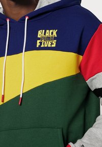 Felpa colorata con un mix di pannelli blu, giallo, verde e rosso. Presenta il logo "BLACK PUMA FIVES" in giallo. Include i lacci.