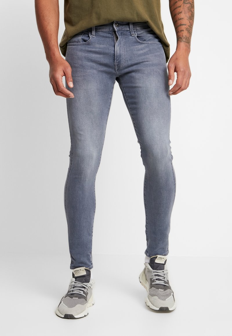 Jeans ajustados de un azul claro con un acabado desgastado, diseño de cinco bolsillos, detalles de desgaste sutil, combinados con zapatillas deportivas grises.