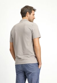 Polo shirt beige a maniche corte realizzato in morbido cotone, caratterizzato da un colletto classico e una vestibilità rilassata, abbinato a pantaloni casual blu in lino.