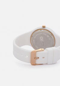 Reloj de silicona blanca con caja redonda de acero inoxidable, acentos en oro rosa en el cierre y la corona, mostrando la parte posterior con la marca de la marca.