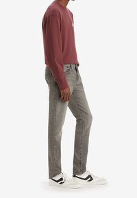 Långärmad mörkröd tröja med rund halsringning, kombinerad med grå jeans och vita sneakers med svarta detaljer.