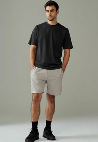 Camiseta de algodón negra combinada con pantalones cortos gris claro. El modelo lleva zapatillas negras y calcetines. Diseño sencillo con un ajuste relajado.