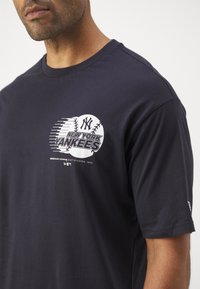 Navy blue cotton t-shirt featuring a white graphic of a baseball and text "NEW YORK YANKEES," with short sleeves and crew neckline.