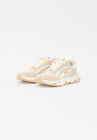 Scarpe da ginnastica beige e bianche con tomaia in suede e rete testurizzata, suole in gomma spesse e lacci bianchi; presenta il logo del marchio sulla linguetta.
