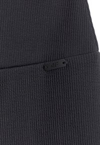 Tissu en tricot côtelé noir plié avec une petite étiquette rectangulaire noire embossée "4F" cousue près du pli.