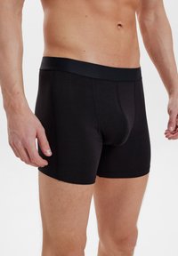 Mustat puuvillaboksarit, joissa on pehmeä joustava vyötärö, muotoilultaan istuva malli ja lyhyt lahkeensuu. Saumadetaljit näkyvissä.