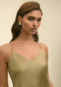 Mouwloze olijfgroene jurk met een V-hals ontwerp, gemaakt van gladde stof. Heeft dunne bandjes en een subtiele textuurafwerking.