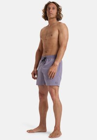 Shorts de bain violets avec un cordon noir, coupe ajustée, texture de tissu lisse et un petit logo visible sur l'ourlet gauche.