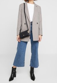 Kostkovaný blázon v neutrálních tónech s dvojitými knoflíky; bílý tričko; světle modré zkrácené džíny; černá crossbody taška; černé kotníkové boty.