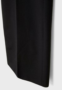 Gros plan d'une jambe de pantalon noire coupe droite avec un ourlet net et une texture de tissu lisse sur un fond clair.