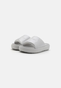 Hvit sandaler med glatt, glossaktig finish. Tykk såle og brede stropper med preget logo-detalj. Teksturerte fotbed for grep.