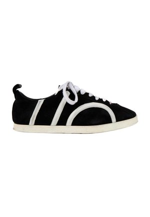 Zapatilla negra de ante con suela blanca, cordones blancos y detalles de rayas blancas curvas y rectas en el lateral.