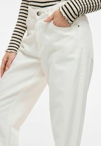 Pantalones blancos de tiro alto hechos de algodón, con cierre de botón, bolsillo lateral y una ligera textura, con un corte relajado.