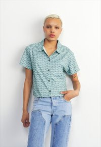 Cămașă cu mânecă scurtă, în teal deschis, cu un model geometric; are un guler și o croială ușor scurtă. Se potrivește cu blugi cu talie înaltă.