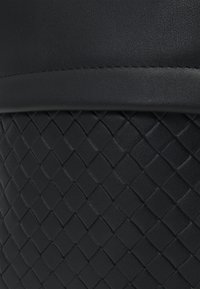 Black leather handbag with a smooth, solid texture at the top and a woven pattern at the bottom. Features a stitched seam for detail.