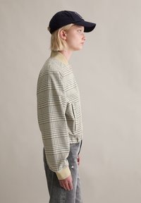 Μπουφάν τύπου bomber με καρό μοτίβο σε μπεζ και ναυτικό μπλε, με ριμπ γιακά και μανσέτες. Διαθέτει πλαϊνή τσέπη και απαλό ύφασμα. Φορεμένο με γκρι τζιν με φθορές.