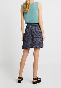 Haut sans manches couleur bleu sarcelle clair associé à une jupe marine à motifs. La jupe est ornée de motifs verticaux et circulaires et possède une taille élastique. Sandales noires.