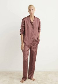 Rustfarvet satin pyjamassæt bestående af en knap-op bluse med krave og løstsiddende bukser, begge med et subtilt blomstermønster.