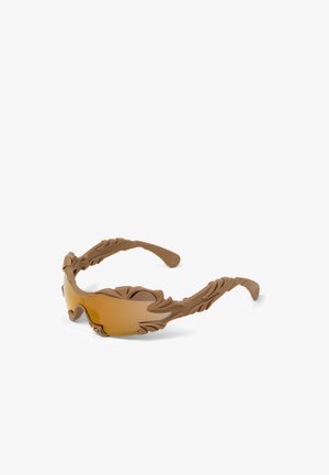 Lunettes de soleil marron avec des montures sculptées texturées en forme de feuille et des verres incurvés teintés ambre, présentées sur fond blanc.