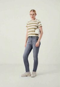 Ριγωτό τοπ σε μπεζ και ελιά, κοντές μανίκες, ψηλόμεσα γκρι τζιν, λευκή τσάντα χειρός και ανοιχτό γκρι sneakers σε ουδέτερο φόντο.