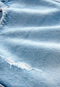 Gros plan d'un tissu en denim bleu clair avec une déchirure effilochée et une couture orange visible près du bord.