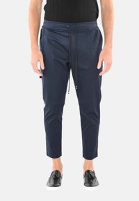 Pantaloni tapered blu navy con cintura elastica, dettagli con cordoncino e tasche laterali. Realizzati in materiale liscio e leggero.