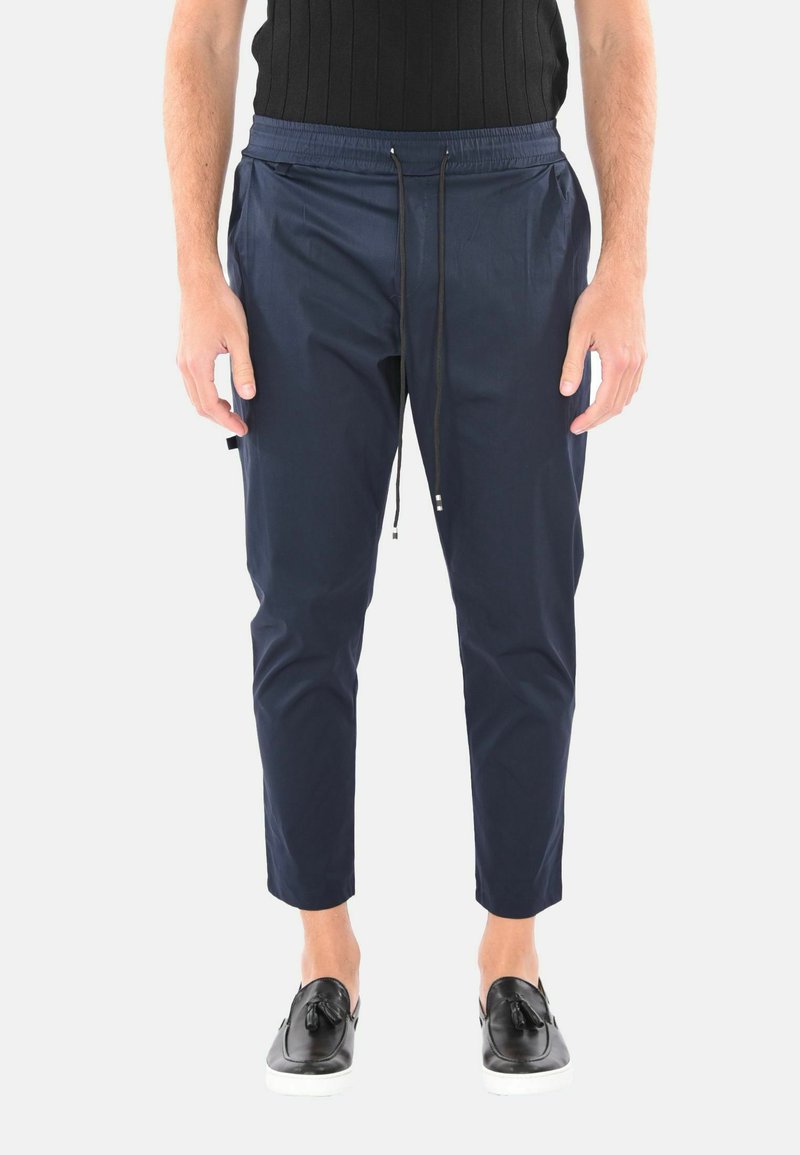 Pantaloni tapered blu navy con cintura elastica, dettagli con cordoncino e tasche laterali. Realizzati in materiale liscio e leggero.