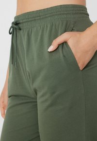 Zelené bavlněné joggery se elastickým pasem, stahovací šňůrkou a bočními kapsami. Hladký povrch s uvolněným střihem.