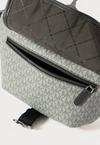 Gray fabric backpack featuring a geometric pattern, a zippered front pocket, and a smooth black trim with a metallic clasp.