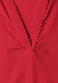 Gros plan d'un décolleté en V en tissu rouge avec des coutures visibles et de légers plis sur le matériau.