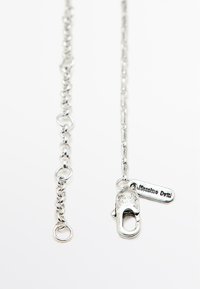 Collana in metallo argento con catena caratterizzata da forme ovali e rotonde interconnesse, dotata di chiusura a moschettone e di un'etichetta con marchio attaccata.