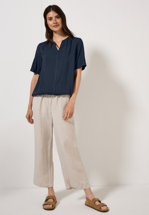 Blusa navy a maniche corte con scollatura a V, abbinata a pantaloni beige chiaro a gamba larga e sandali marroni. Tessuto morbido, vestibilità rilassata.