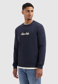 Donkerblauwe sweatshirt van katoen, met een ronde hals, lange mouwen en een wit geborduurd logo op de borst. Geribbelde boorden en onderrand.