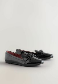 Scarpe da barca in vernice nera con punta arrotondata, dettagli in pizzo e fodera rossa. Suole piatte con un motivo di grip testurizzato.