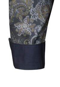 Polsino di camicia blu scuro con un motivo paisley in oro, bianco e grigio. Il tessuto appare setoso, con dettagli intricati e forme fluide.