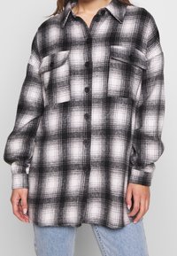 Svart och vit rutigt flanellskjorta med två framfickor, knäppning framtill och långa ärmar. Mjuk textur, avslappnad passform.
