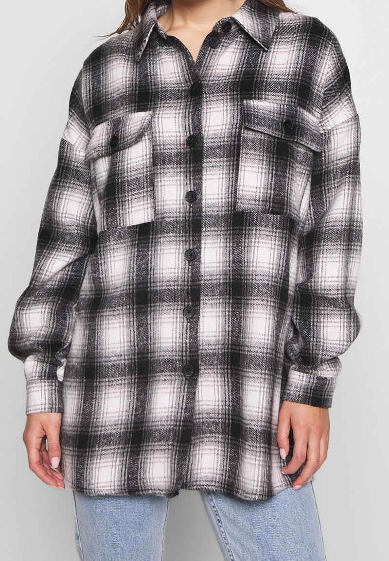Svart och vit rutigt flanellskjorta med två framfickor, knäppning framtill och långa ärmar. Mjuk textur, avslappnad passform.