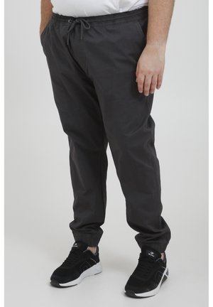 Dark gray, lightweight pants with an elastic waistband and adjustable drawstring. Tapered leg fit, paired with black sneakers.