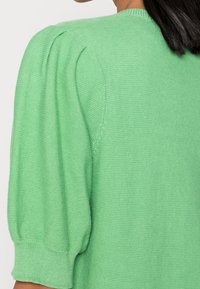 Zelený pletený svetr s krátkými balónkovými rukávy, kulatým výstřihem a texturovaným vzorem látky.