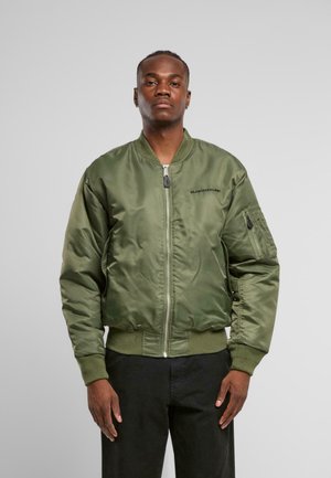 Olivgrüne Satin-Bomberjacke mit Reißverschluss, gerippten Bündchen und Saum. Verfügt über eine seitliche Tasche mit Reißverschluss und schwarzem Logo auf der Brust.