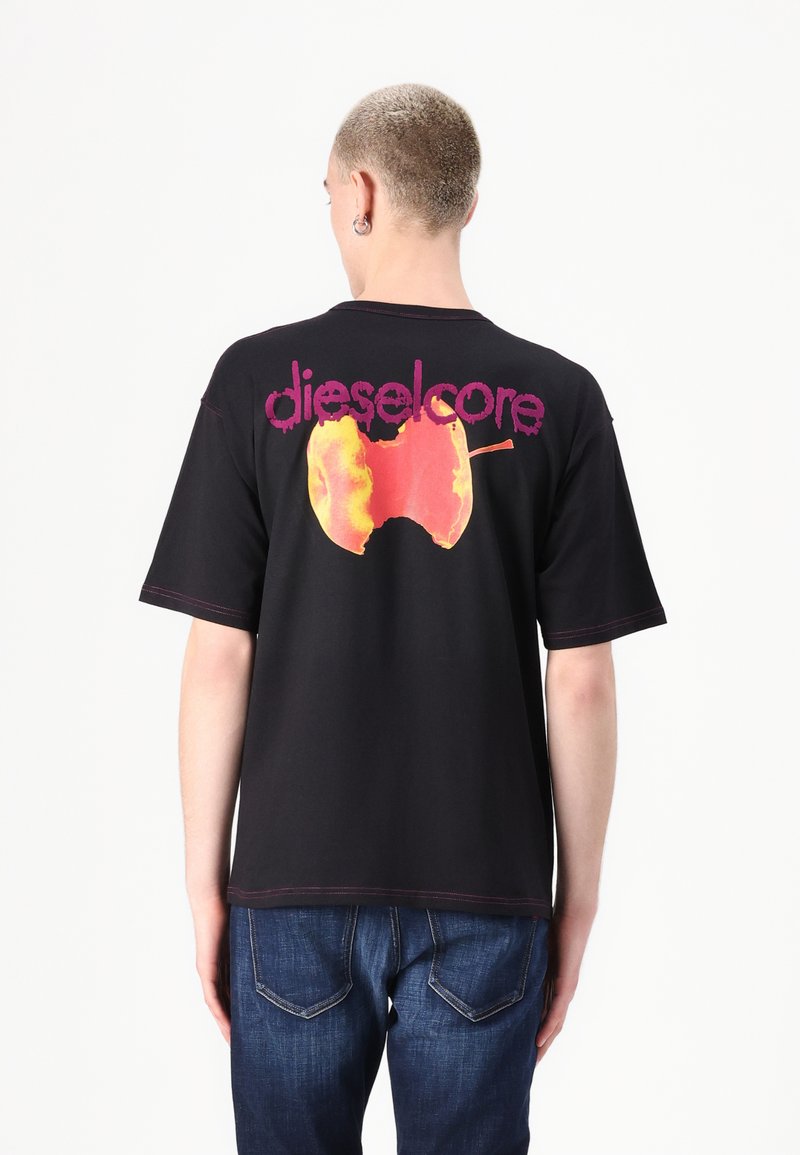 T-shirt en coton noir avec un grand graphique de pomme orange et jaune, portant le texte "dieselcore" au-dessus, le tout complété par des bords cousus contrastants.