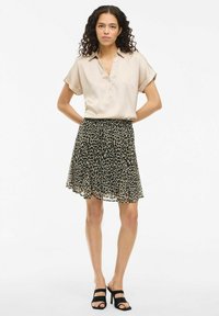 Blouse beige à manches courtes avec un pli de boutons, associée à une mini-jupe à imprimé léopard noir. Des talons à lanières noirs complètent le look.