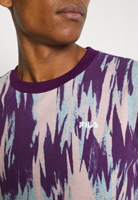 T-shirt à manches courtes en tissu doux, présentant un motif abstrait violet et bleu, avec un col côtelé violet contrastant et un logo blanc.