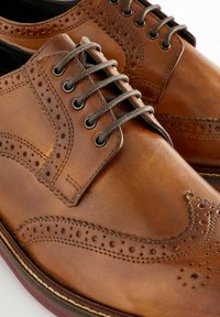 Pantofi din piele maro cu șireturi, având detalii brogue, suprafață texturată, cusături contrastante și gauri metalice rotunde pentru șireturi.