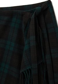 Écharpe à carreaux en mélange de laine douce, avec des couleurs vert foncé et noir, des bords frangés, et un design noué pour un port sécurisé.