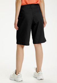 Black knee-length shorts with a smooth texture, a flat waistband, and back pockets. Worn with white athletic shoes.