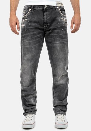 Jean en denim gris foncé avec une finition délavée, cinq poches et des coutures contrastantes. Associés à des baskets blanches pour le contraste.