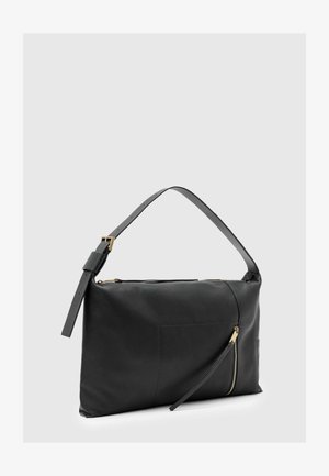 Sac à épaule en cuir noir avec sangle réglable, boucle dorée et poche zippée en diagonale à l'avant sur un fond gris clair uni.