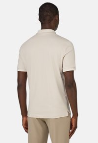 Beige pikétröja i mjukt tyg, med korta ärmar, vikad krage och sprund i sidorna för ökad rörelsefrihet.