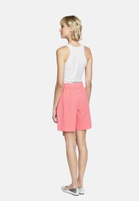 Różowe lniane szorty z elastycznym paskiem w talii, zestawione z białą bluzką bez rękawów, widok z tyłu, podkreślający prosty design.